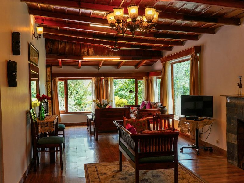 A rustic living room with wooden ceiling beams, a chandelier, and large windows