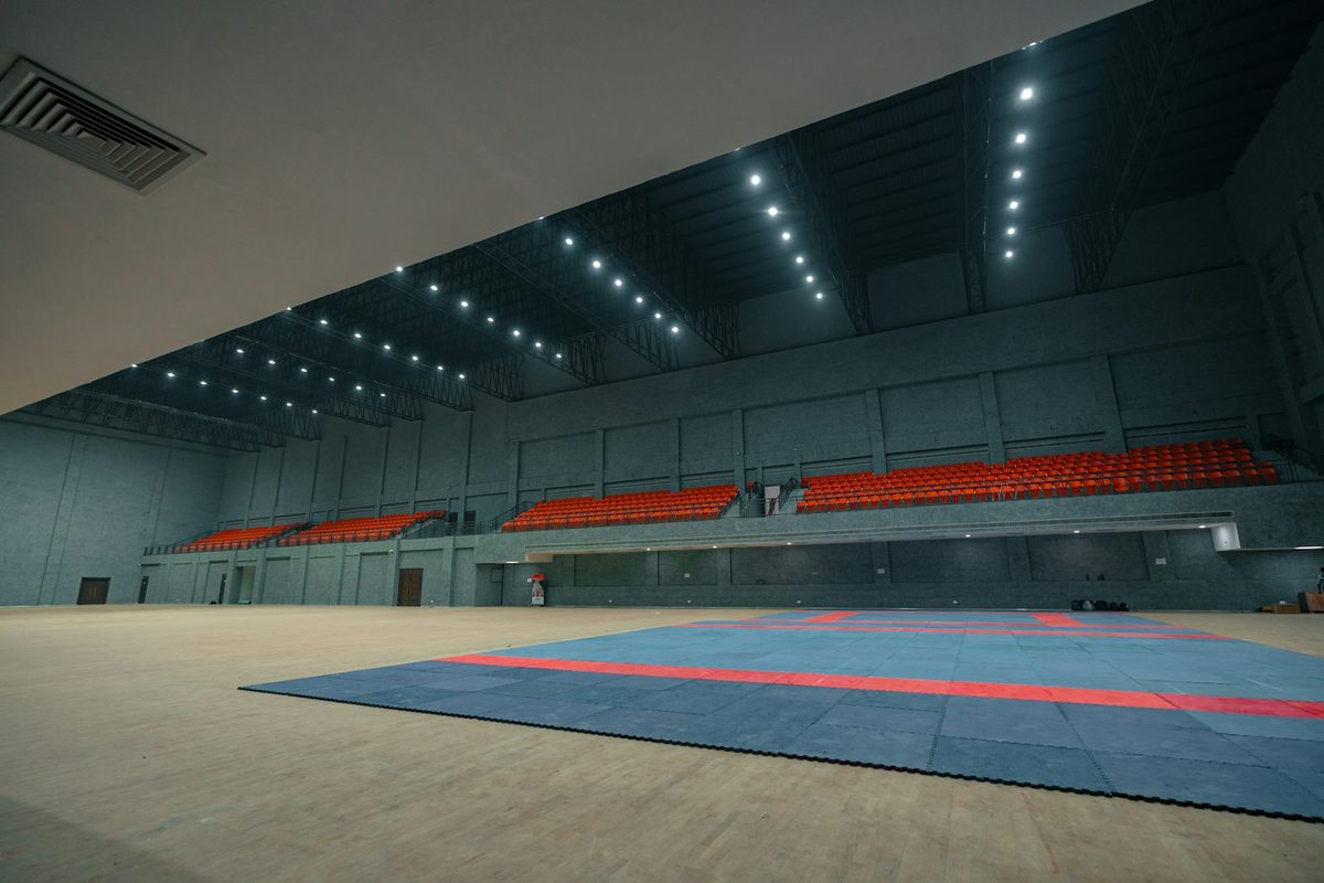 Empty indoor sports arena with red seating and blue mats