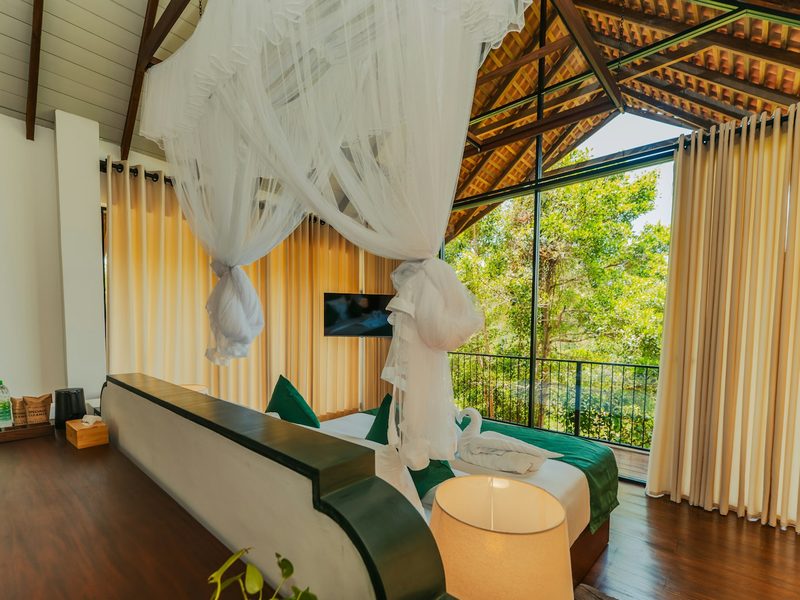 A hotel bedroom with a canopy bed and large windows overlooking lush green trees