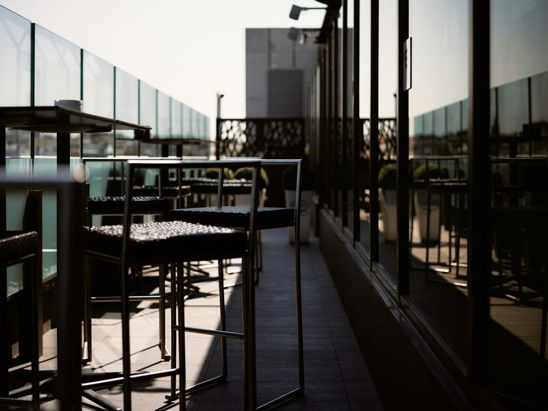 High bar stools on a rooftop terrace with glass railings in low light