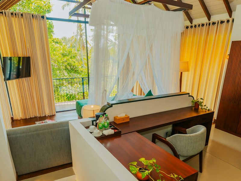 A hotel room with a canopy bed, a wooden desk, and a balcony overlooking trees