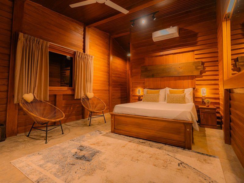 A bedroom with wooden walls, a double bed, and two round wicker chairs