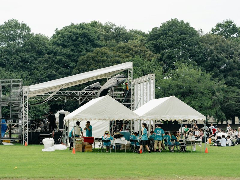 A stage and white tents on a grassy field with people gathered nearby